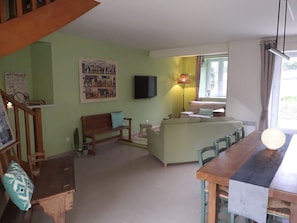 Un salon chaleureux avec un banc en bois, un canapé, une table à manger et un téléviseur fixé au mur.