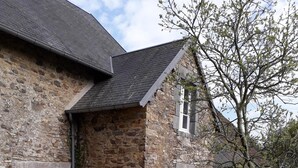 Ein Steinhaus mit Ziegeldach, einem Holztisch mit Stühlen und einem Baum im Hof.