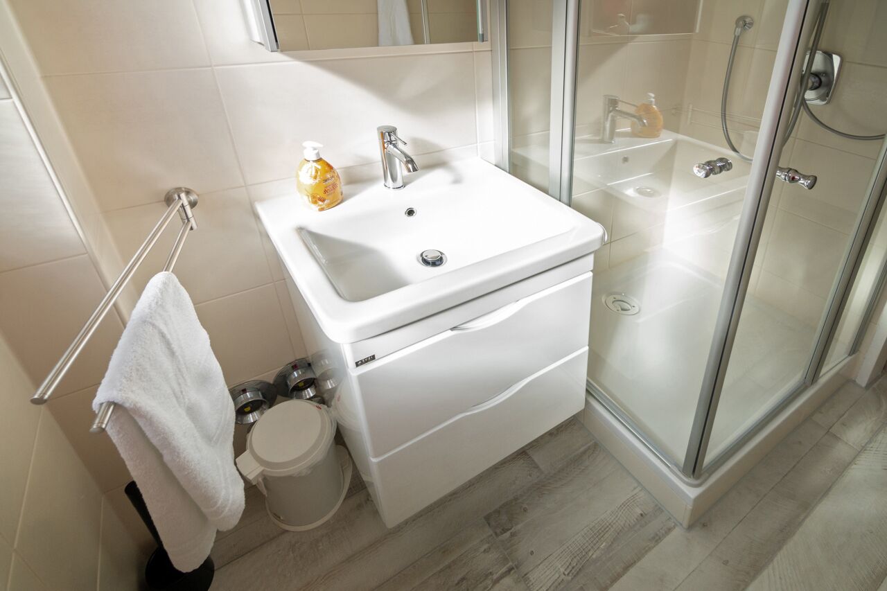 A modern bathroom with a white sink, a glass shower enclosure, and a towel rack.