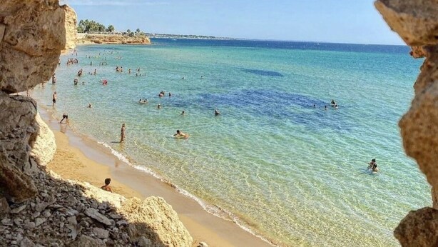 Une plage bordée d’une eau turquoise et limpide, visible à travers l’entrée d’une grotte rocheuse.