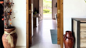 Un couloir avec une porte en bois donnant sur une pièce, une plante en pot et un vase posé sur le sol.