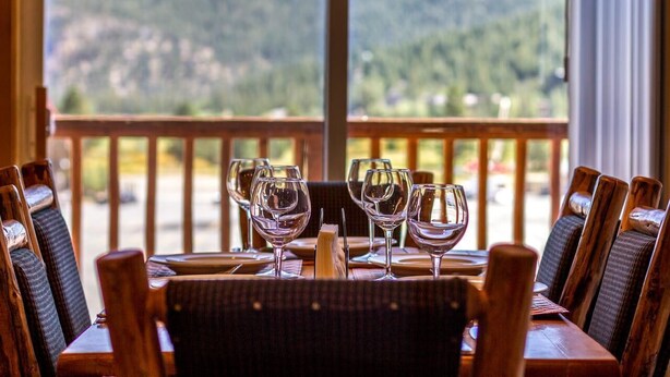 Mesa de comedor con cuatro copas de vino y un menú, frente a una vista panorámica de montañas.