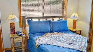 Un dormitorio con cama, dos mesitas de noche, una ventana con persianas y una colcha estampada.
