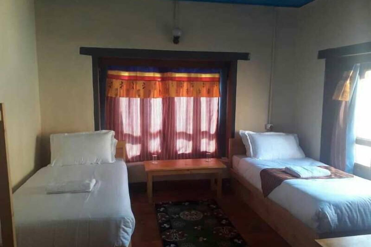 A room with two single beds, a small table, and a window with curtains.
