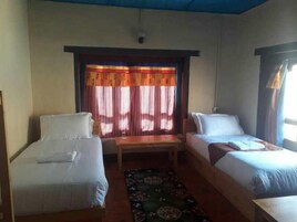Una habitación con dos camas individuales, una mesita y una ventana con cortinas.