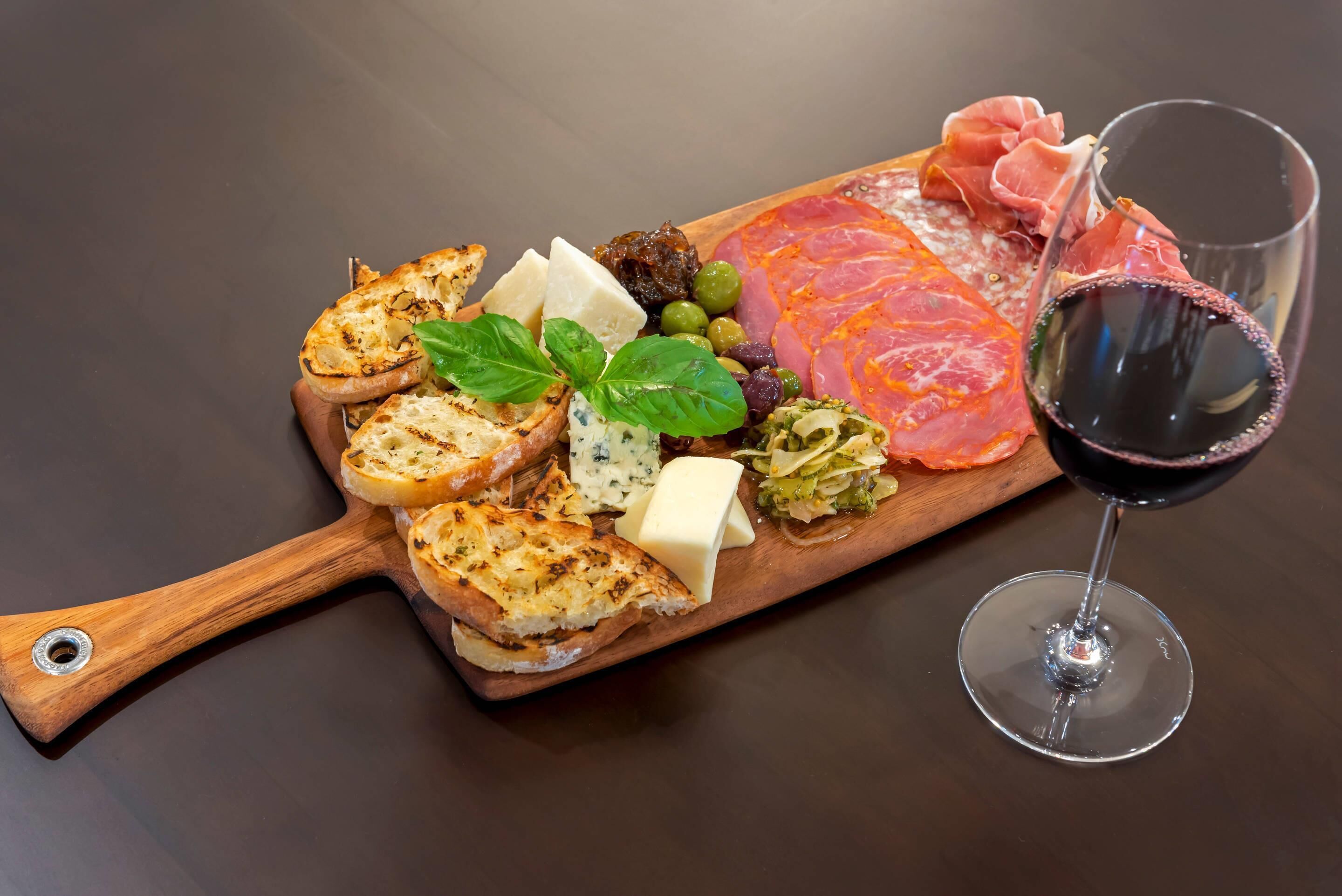 Eine Platte mit verschiedenen Käsesorten, Wurstwaren, Oliven und Brot, dazu ein Glas Rotwein.