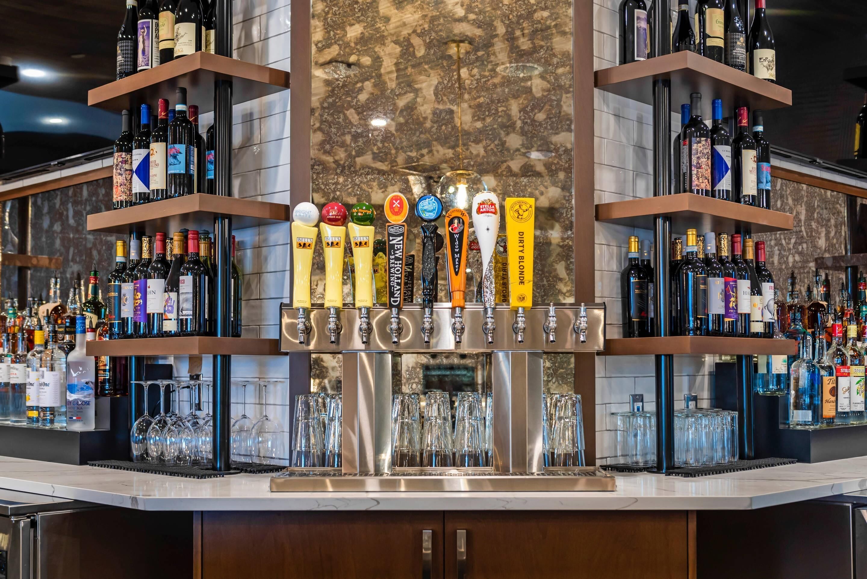 A bar area with multiple shelves of bottled beverages and a tap system with various beer taps.