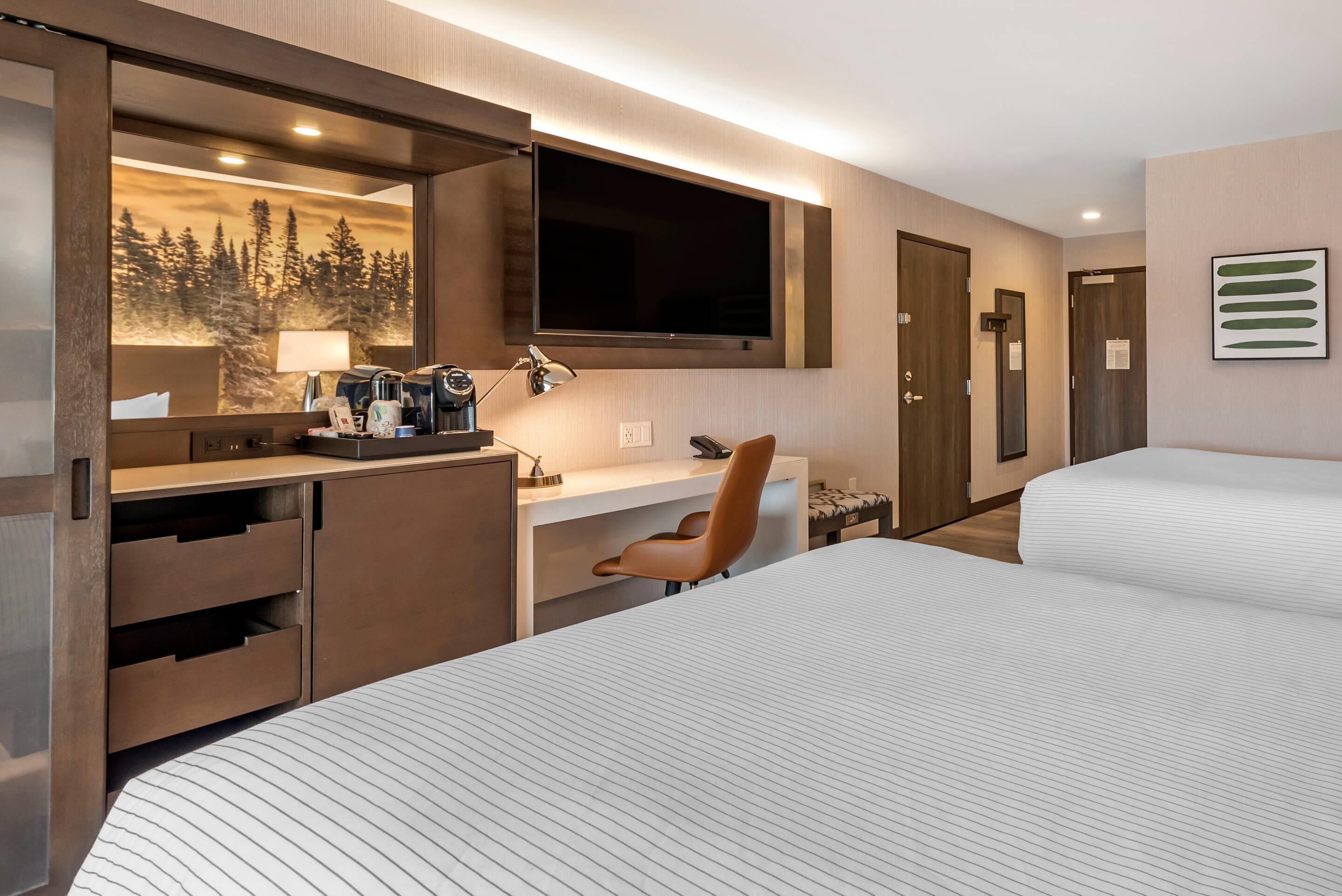 Ein Hotelzimmer mit Bett, Schreibtisch, Computer, Sessel, Fernseher und Spiegel.
