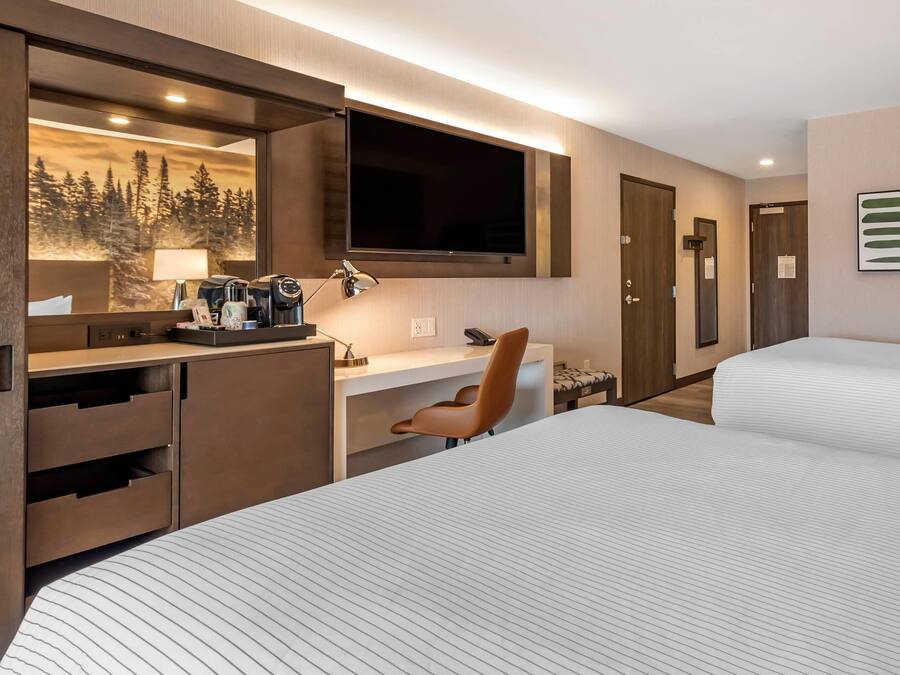 Una habitación de hotel con una cama, un escritorio con computadora, una silla, un televisor y un espejo.