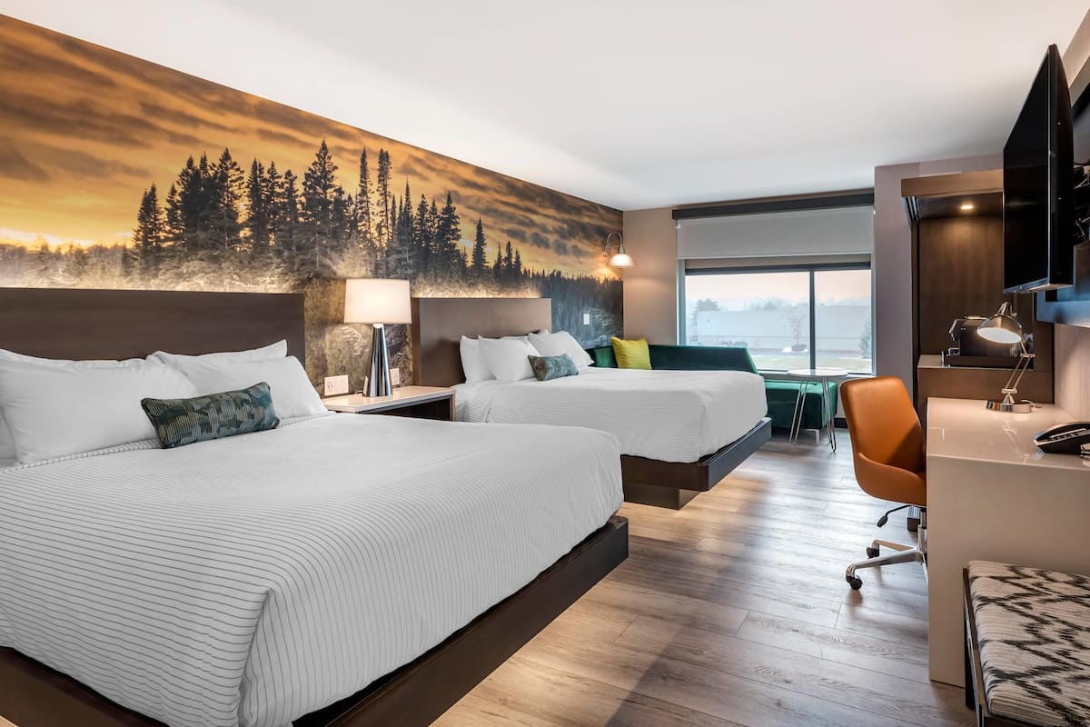 A hotel room with two beds, a desk, a chair, and a large window.