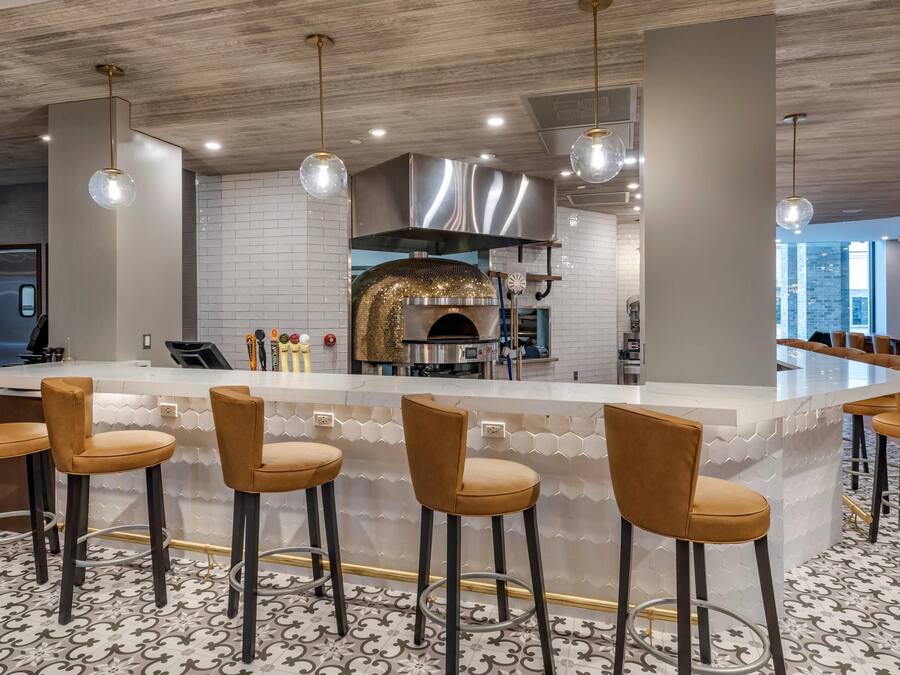 A modern kitchen with a built-in oven, bar stools, and pendant lighting.