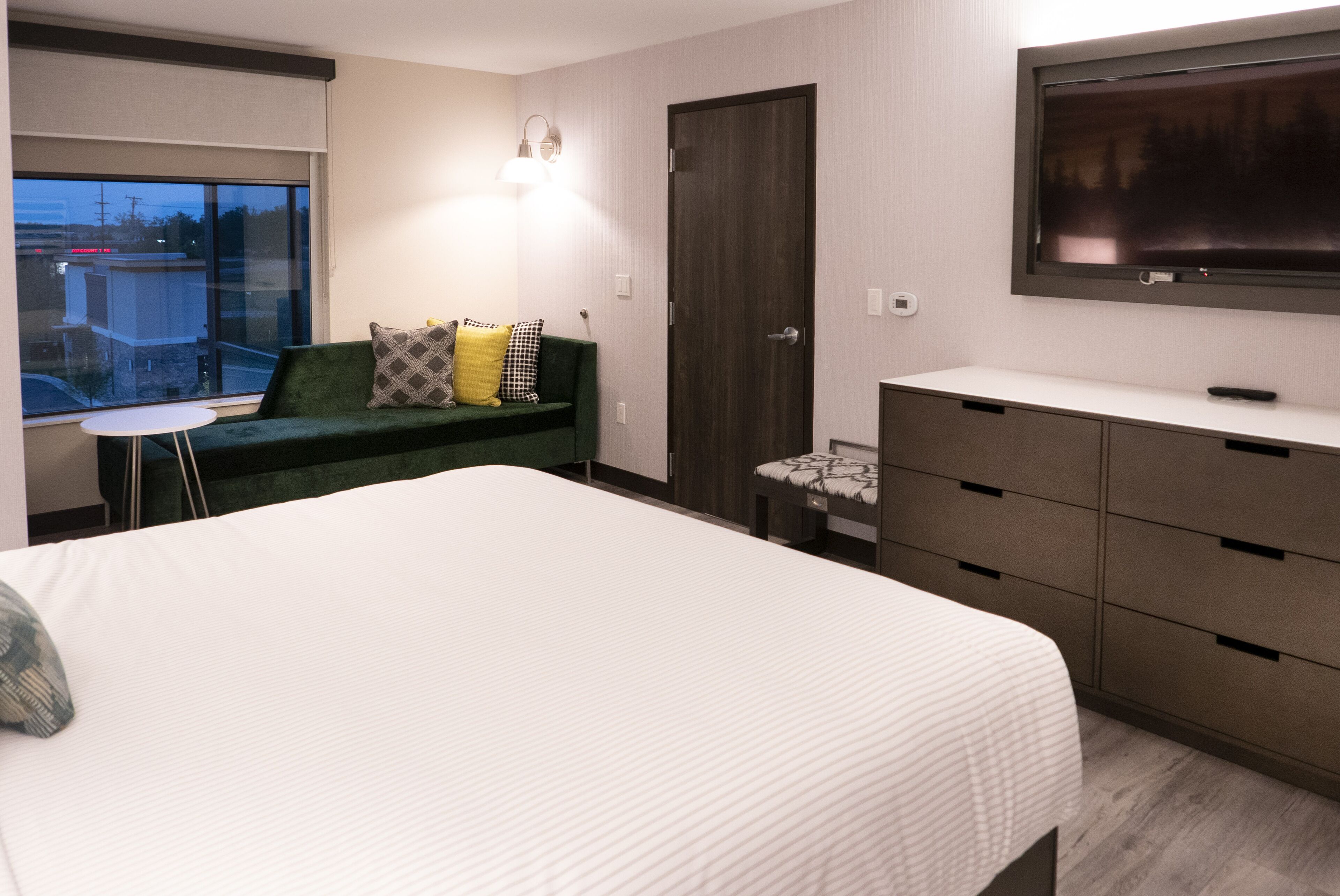 A bedroom with a large bed, a green sofa, a TV mounted on the wall, and a dresser.
