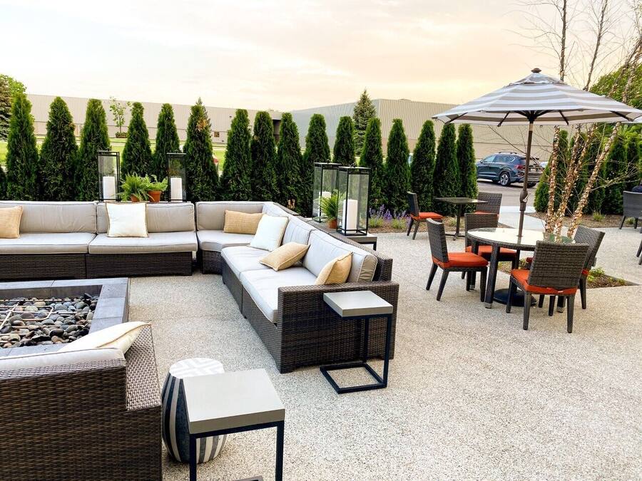 Een terras met een loungebank, een ronde tafel met stoelen, een vuurkorf en een grote parasol.