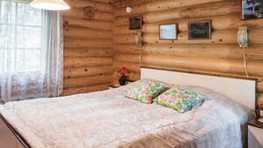 A log cabin bedroom with a bed, floral pillows, a nightstand, a clock, and framed pictures on the wall.