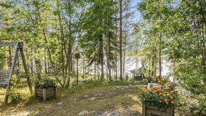 A forested area with a wooden bench, a wooden planter with flowers, and a gazebo.