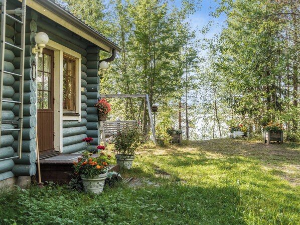 A log cabin with a porch, surrounded by a garden with various plants and flowers.