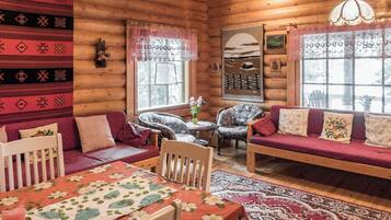 Ein gemütliches Blockhaus-Interieur mit Esstisch, zwei Sofas und einem kleinen runden Tisch.