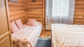 Ein gemütliches Blockhauszimmer mit Holzvertäfelung, einem Bett mit Blumenmusterdecke, einem Fenster mit durchsichtigen Vorhängen und einer kleinen Pflanze an der Wand.