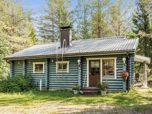 Une cabane en rondins avec une cheminée, des fenêtres et une véranda agrémentée de plantes en pot.