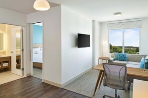 A hotel room with a bed, a desk with a chair, a TV, a sofa, and a window with a view. - Element by Marriott Hampton Peninsula Town Center (Hampton)