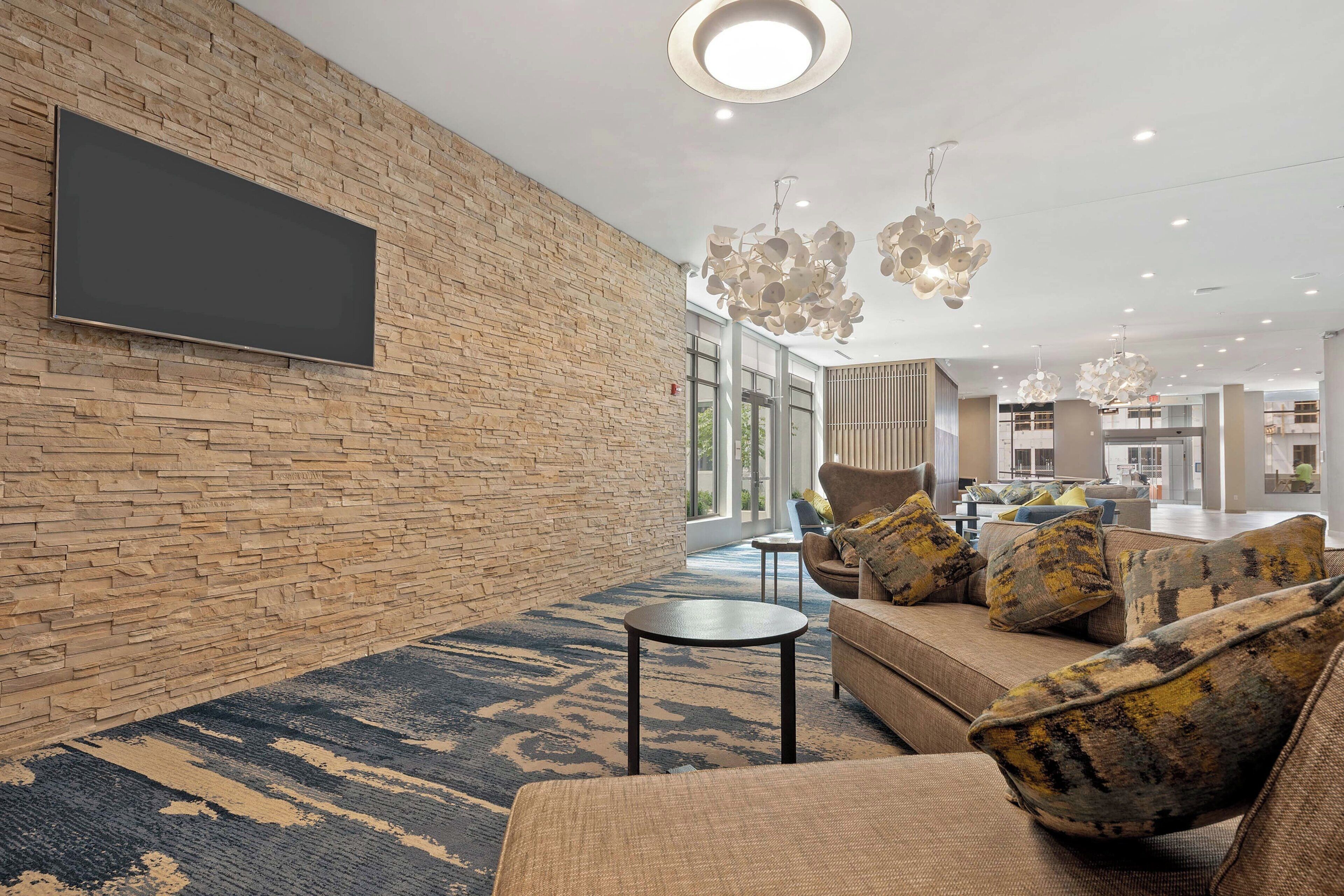 Un vestíbulo moderno con pared de piedra, televisor de pantalla plana, sofá con cojines estampados y alfombra azul.