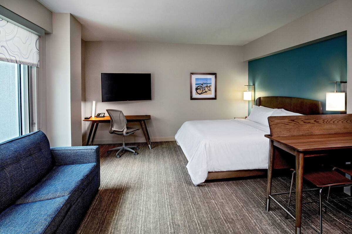 A hotel room with a bed, a desk with a chair, a television, and a sofa.