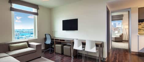 Une chambre d’hôtel moderne dotée d’une grande fenêtre, d’un canapé, d’un bureau avec des chaises et d’un téléviseur à écran plat.