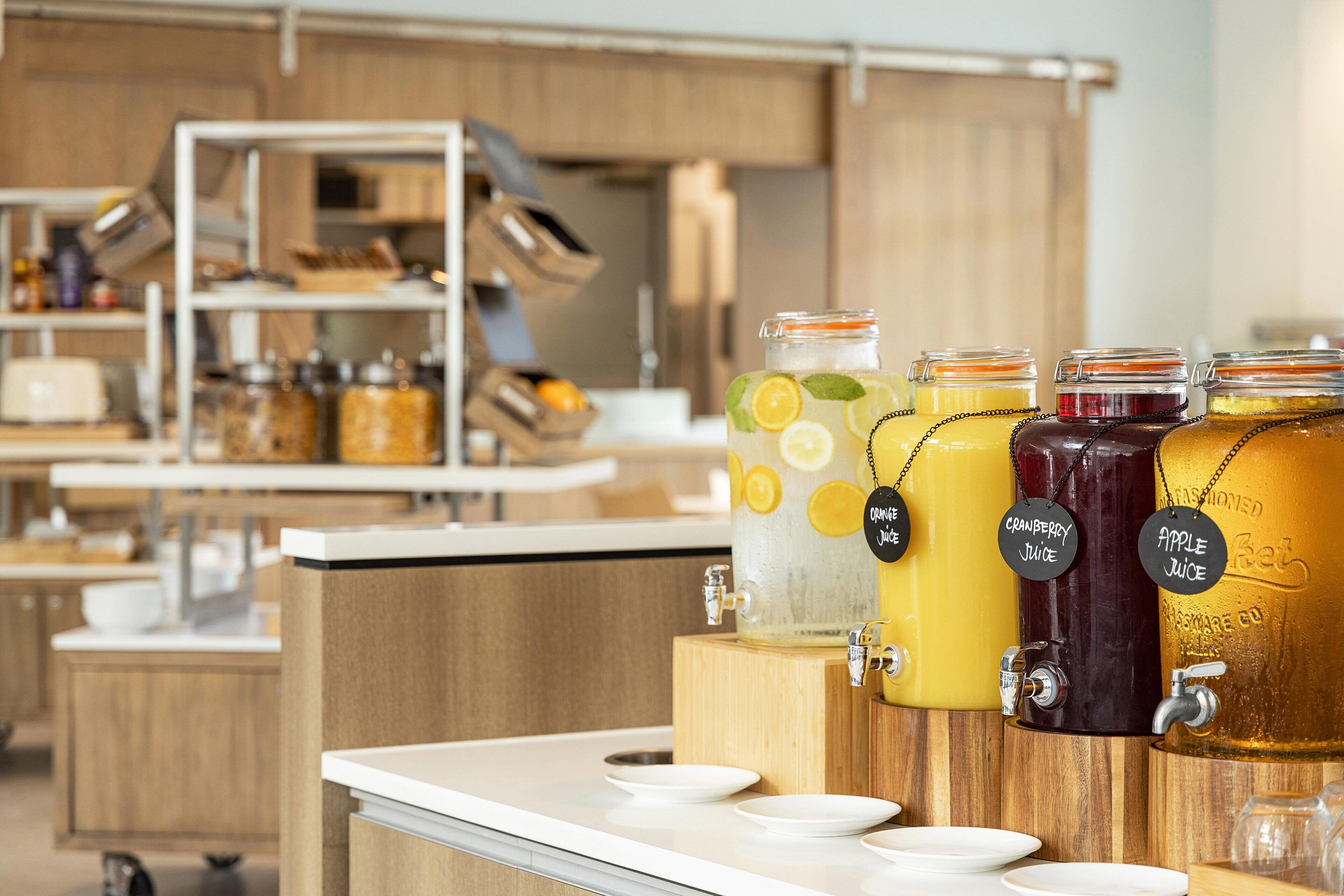 A beverage station with various fruit juices, including lemon, cranberry, and apple, in a modern kitchen setting.