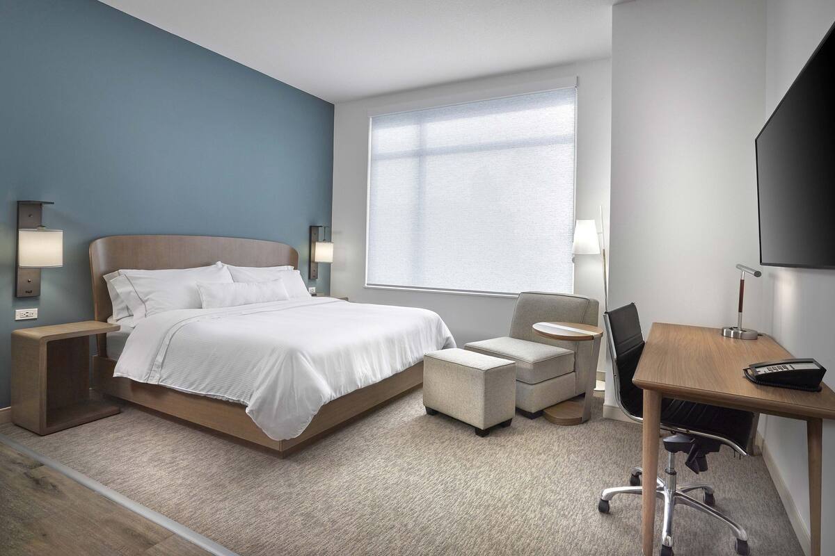 A hotel room with a bed, a desk, a chair, a TV, and a window.