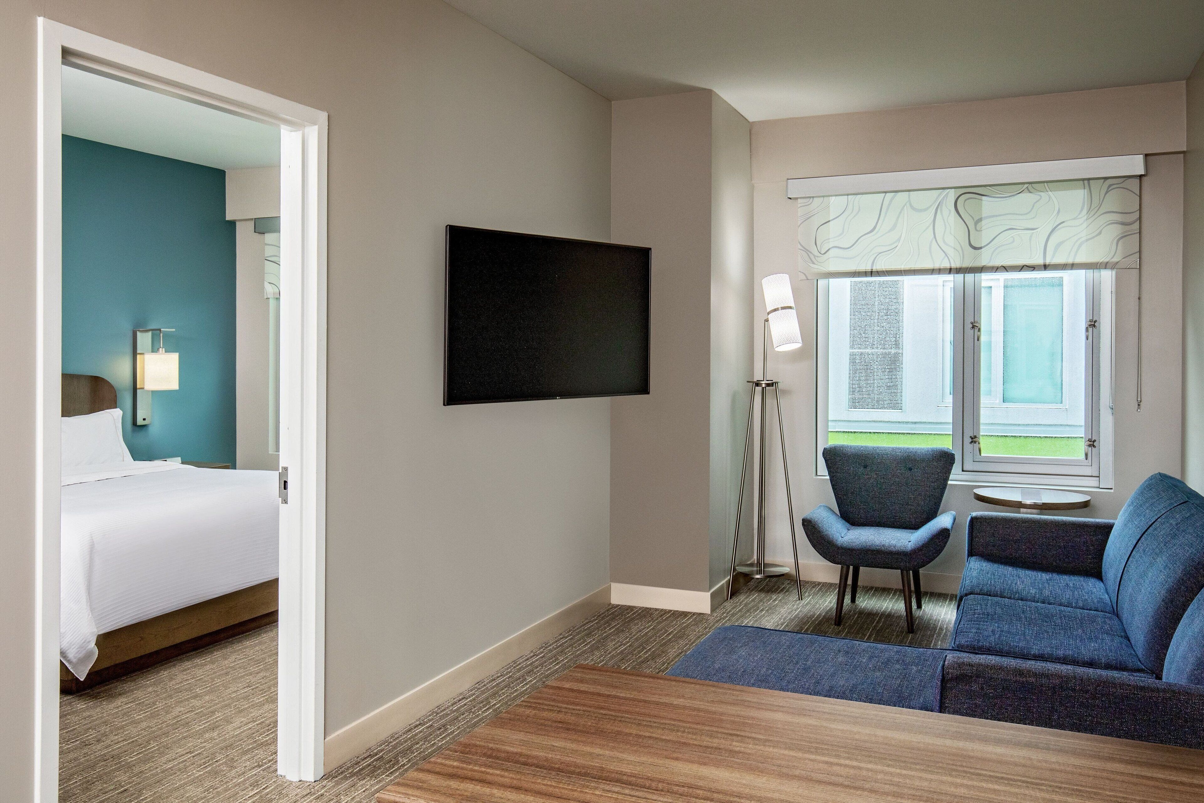 A hotel room with a bed, a sofa, a TV, a lamp, and a window with a view.