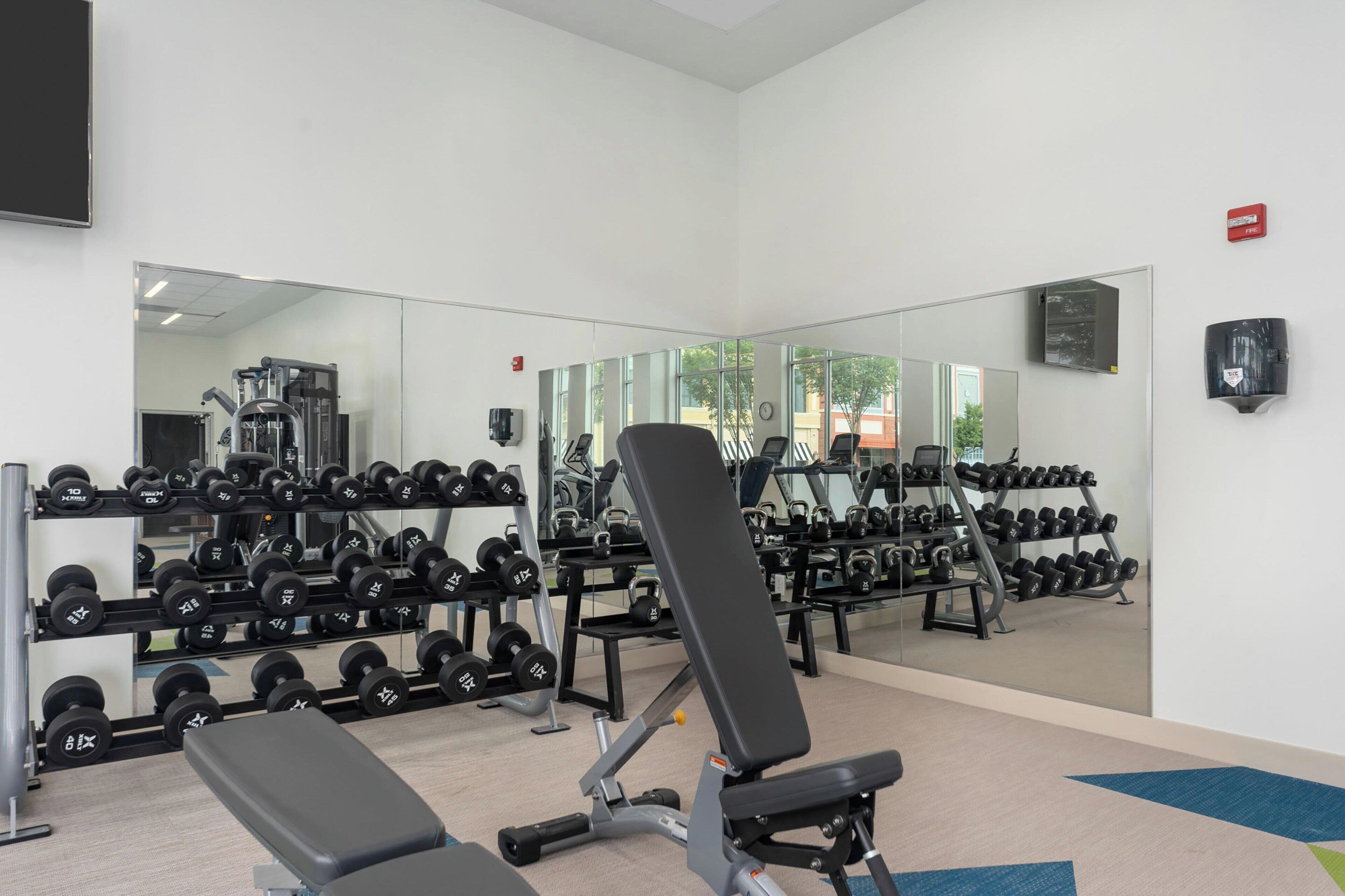 A gym with weightlifting equipment, mirrors, and a bench.