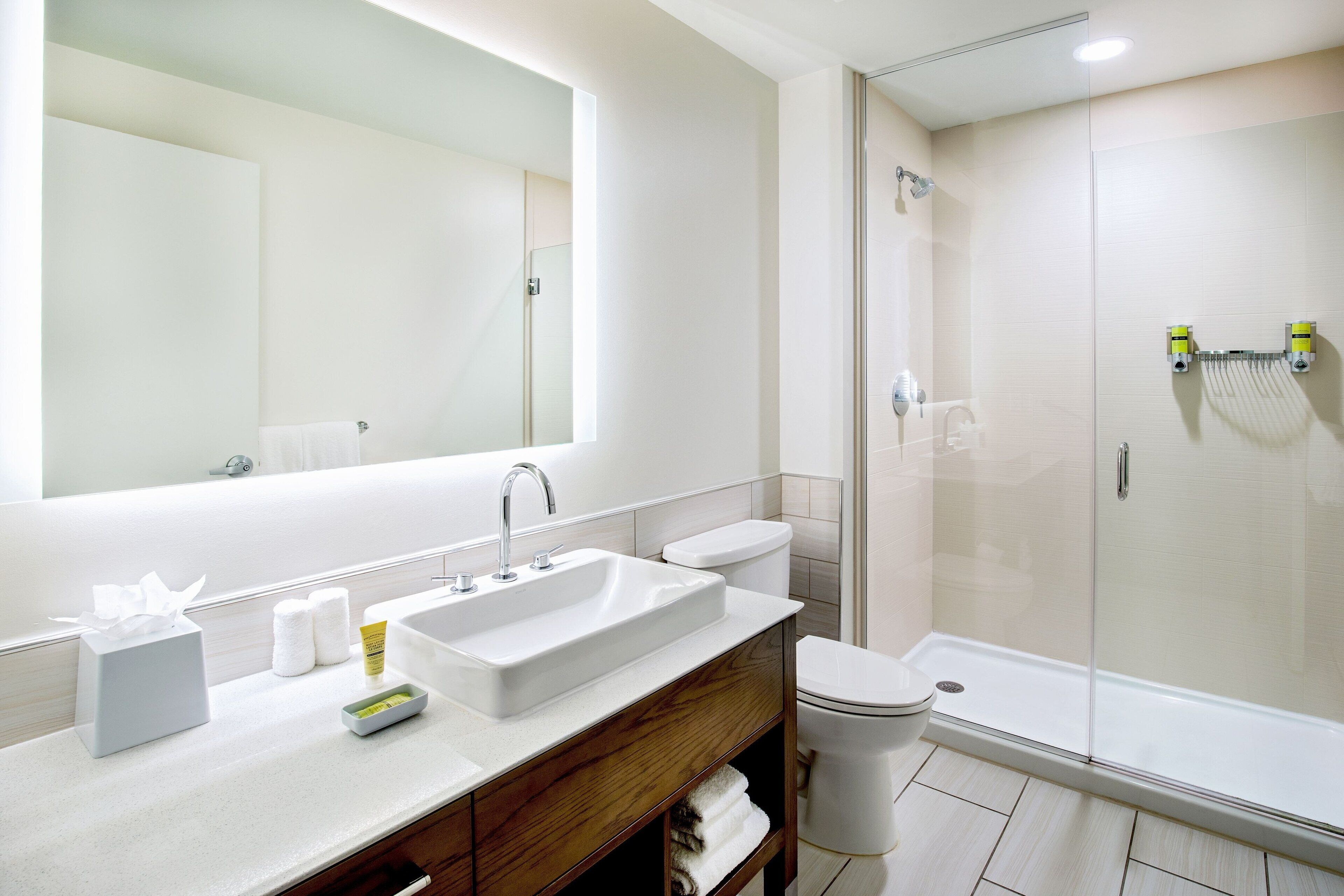 Un baño moderno con un espejo grande, un lavamanos, un inodoro y una ducha con mampara de vidrio.