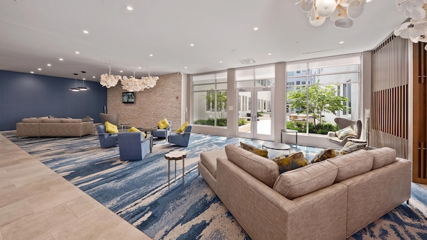 Um lobby moderno com esquema de cores azul e bege, apresentando um grande sofá, poltronas, uma mesa de centro e um tapete estampado.