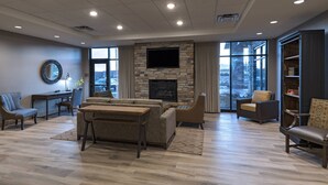 A spacious living room with a stone fireplace, comfortable seating, and a large window offering a view of the city. - Fairfield Inn & Suites by Marriott Colorado Springs East/Ballpark (Colorado Springs)