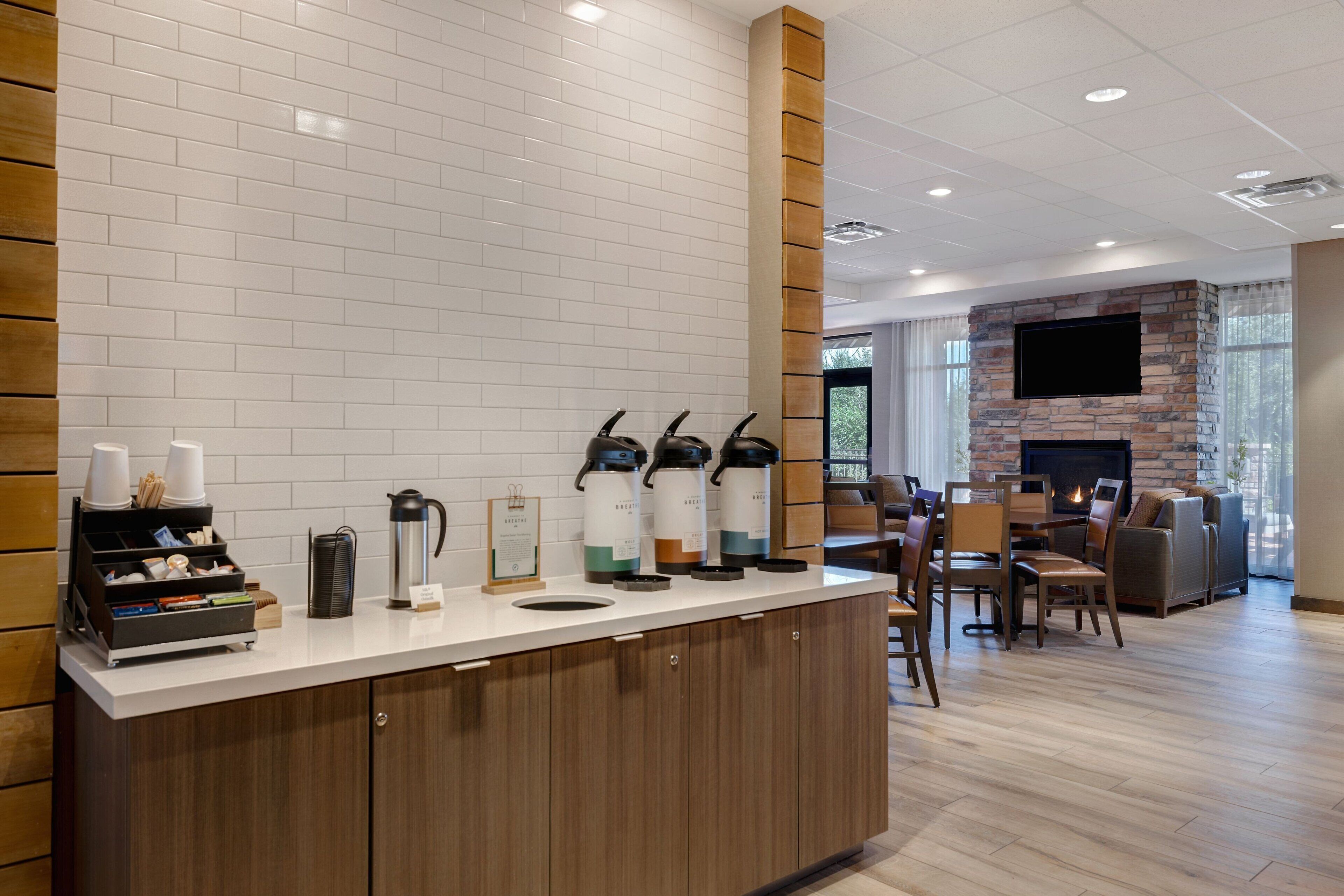 Um hall de hotel moderno com um canto de café, área de estar e lareira.