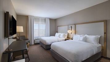 A hotel room with two beds, a desk, a TV, and a window with curtains.