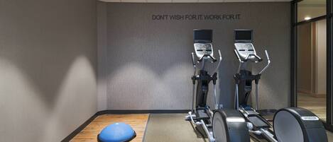 A gym with two elliptical machines and a blue balance ball, a motivational quote on the wall, and a wooden floor.