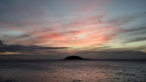 Un coucher de soleil sur une mer calme, avec une petite île à l'horizon.