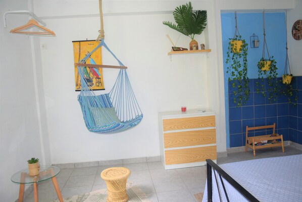A room with a bed, a hanging chair, a small table, and a wooden bench.
