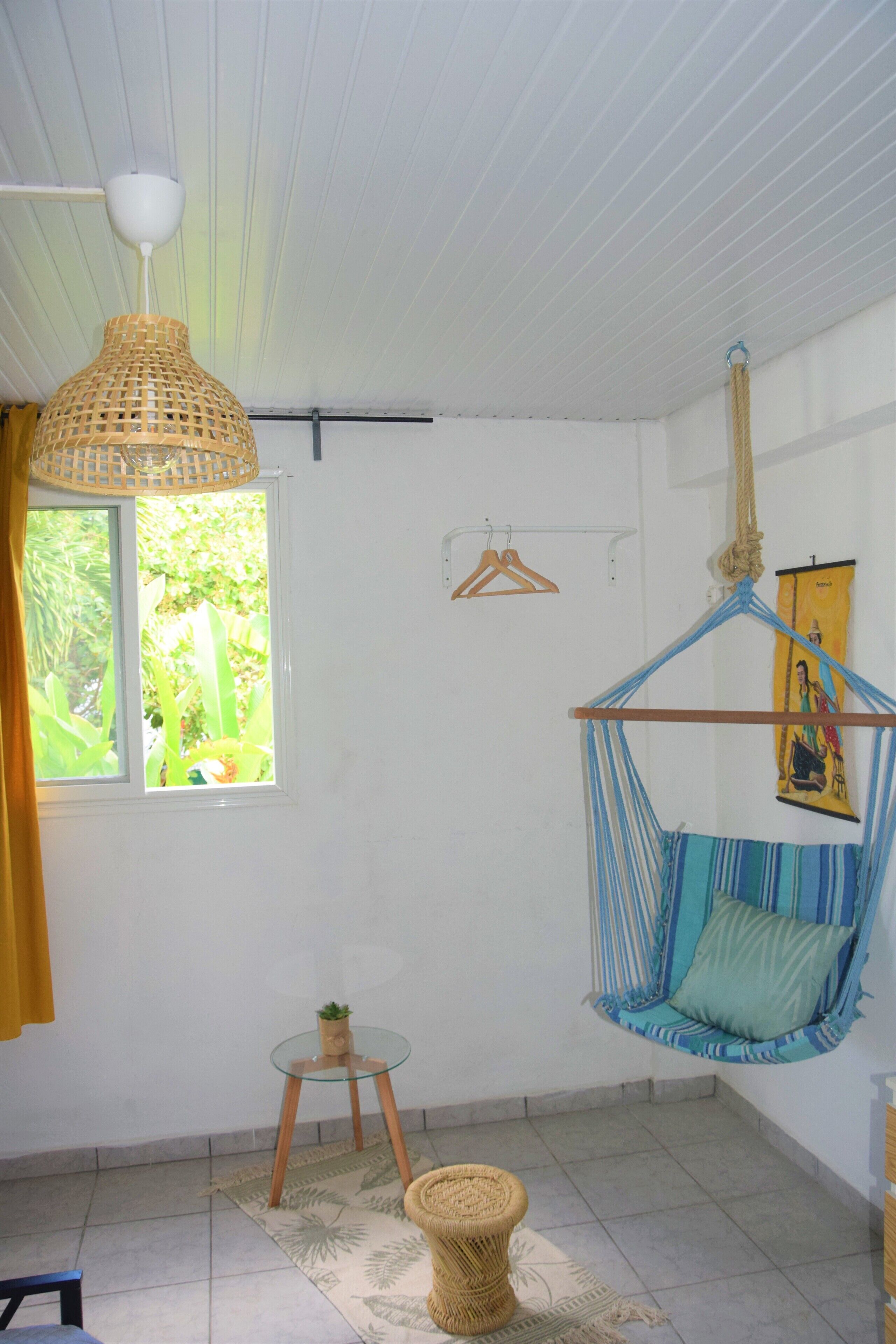 Una habitación con una hamaca colgante, una mesita y un ventanal con vistas a la vegetación.