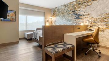 A modern room with a wooden desk, a cushioned chair, a bed, and a brick wall.