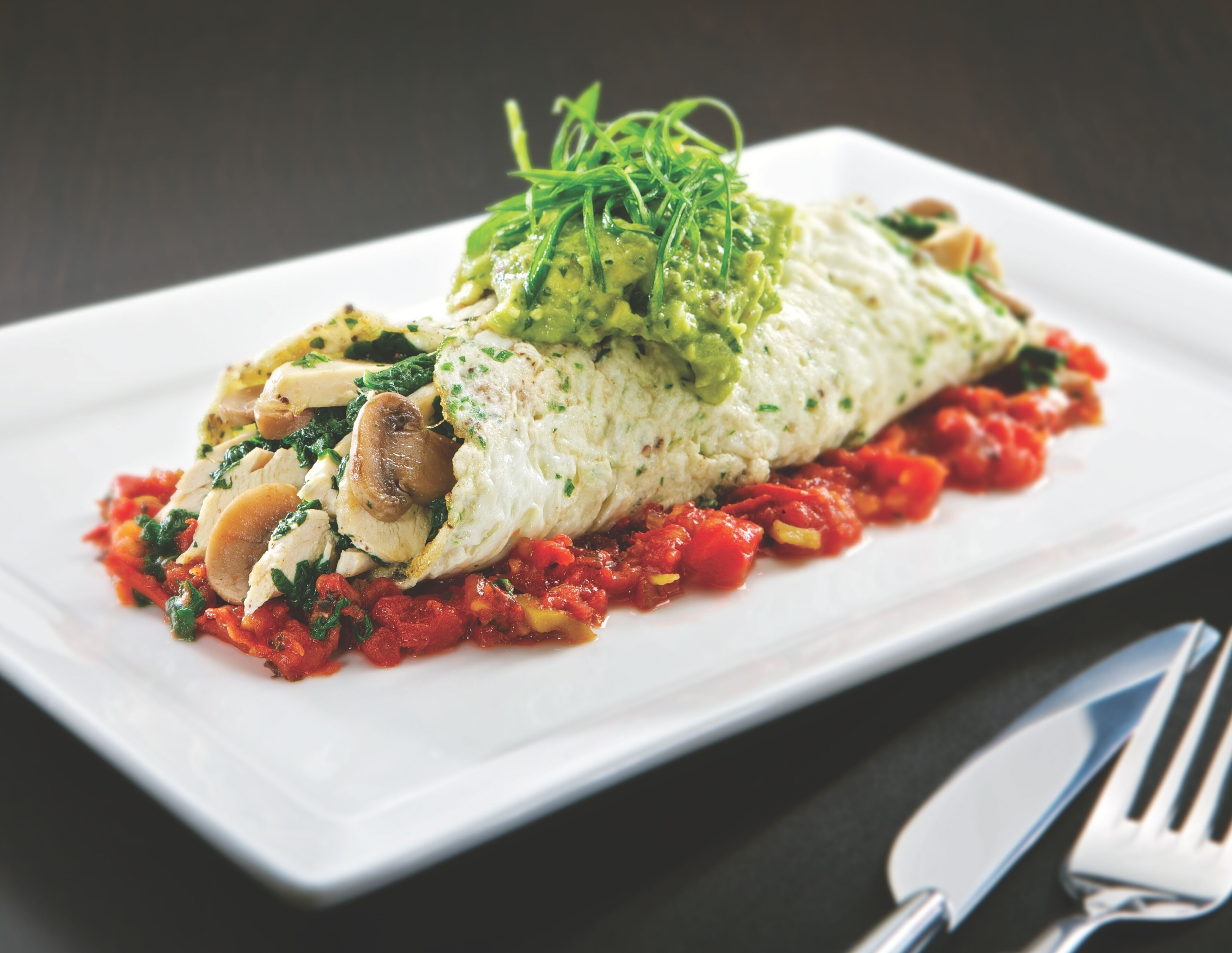 Ein Teller Essen mit einer gerollten Omelett, Pilzen und einer Tomatensoße.