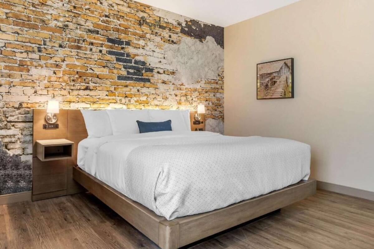 Ein Schlafzimmer mit Backsteinwand, einem Bett mit weißer Bettwäsche, zwei Nachttischen mit Lampen und einem gerahmten Bild an der Wand.