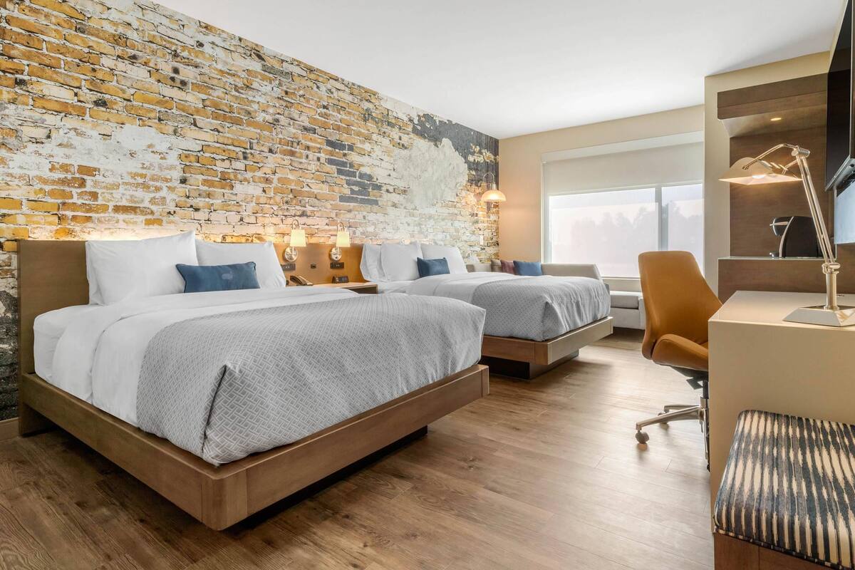 Ein modernes Hotelzimmer mit zwei Betten, einer Ziegelwand, Holzboden und einem Schreibtisch mit Stuhl.