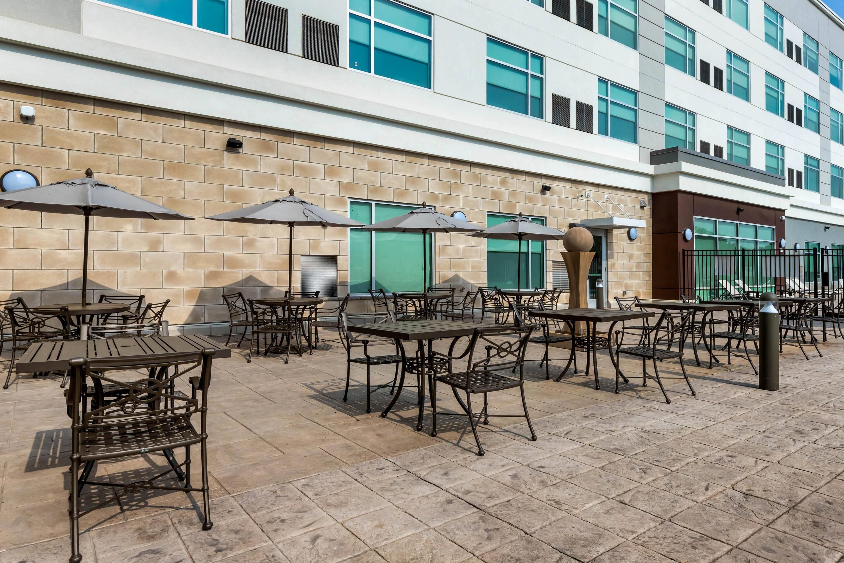 An outdoor patio area with tables and chairs, umbrellas, and a brick wall.