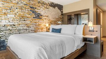 A modern hotel room with a brick wall, a wooden bed frame, and a nightstand with a lamp.