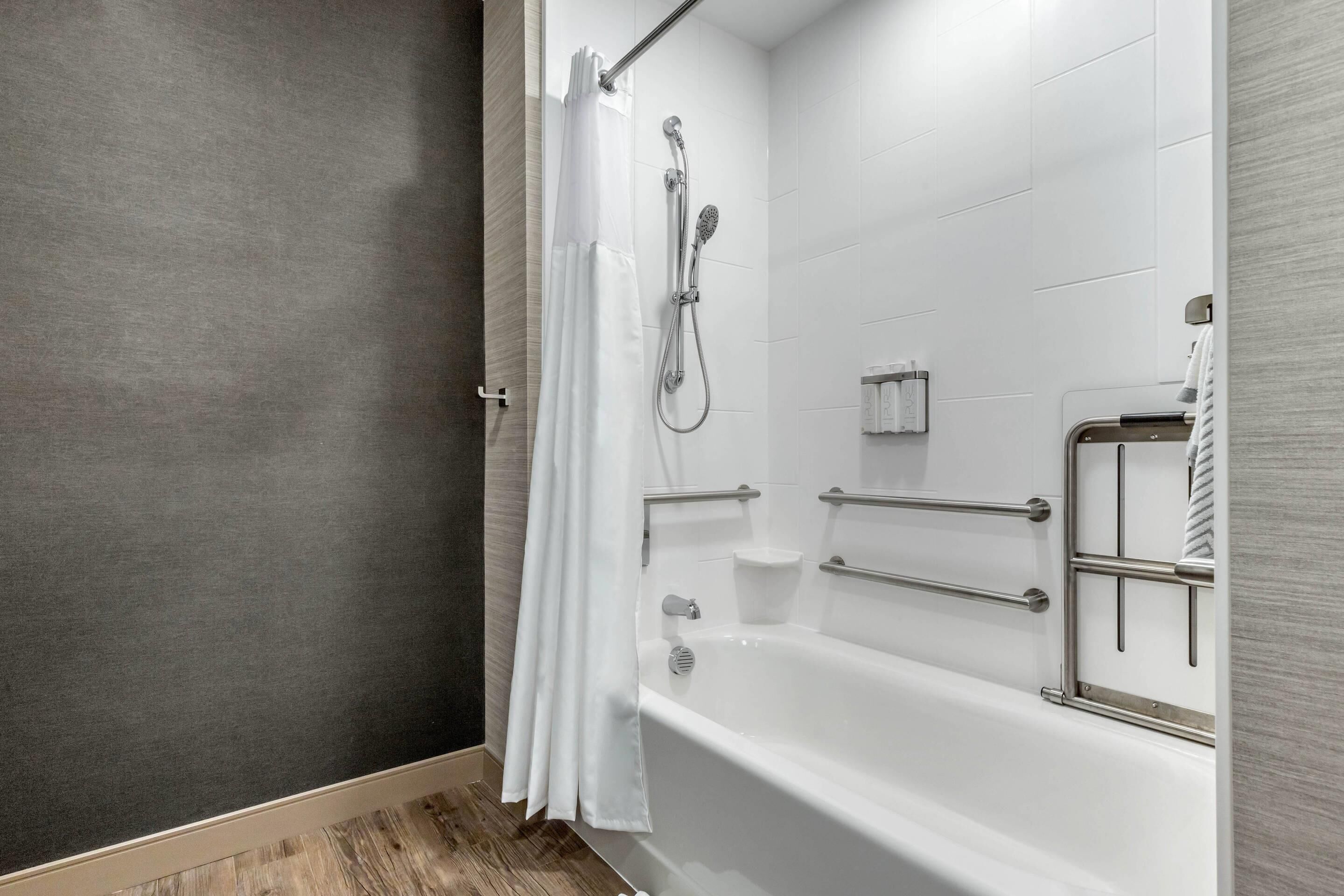 A modern bathroom with a walk-in shower, grab bars, and a white bathtub.