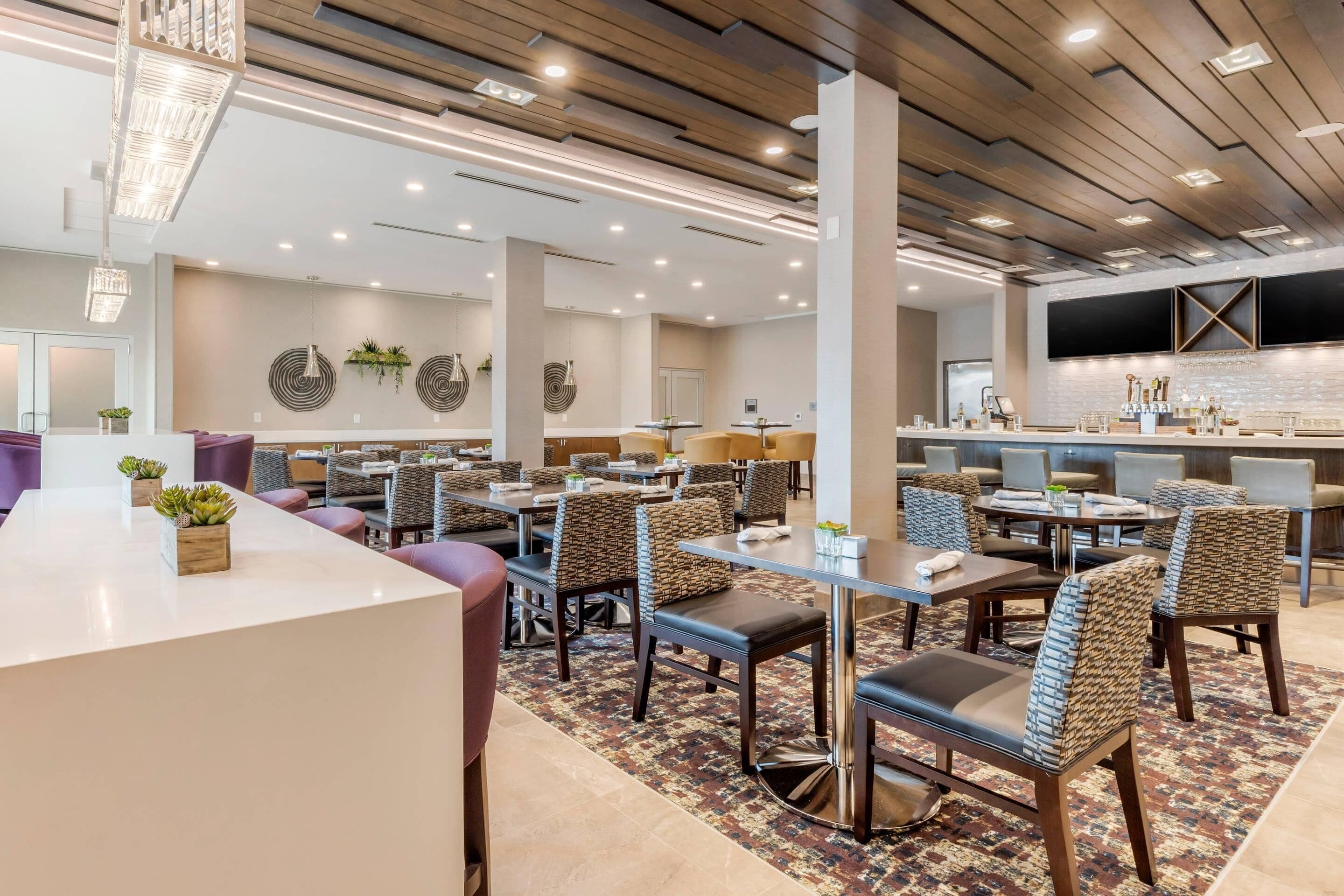 Un hall d’hôtel moderne doté de plusieurs espaces de détente, d’un comptoir d’accueil et d’un bar.