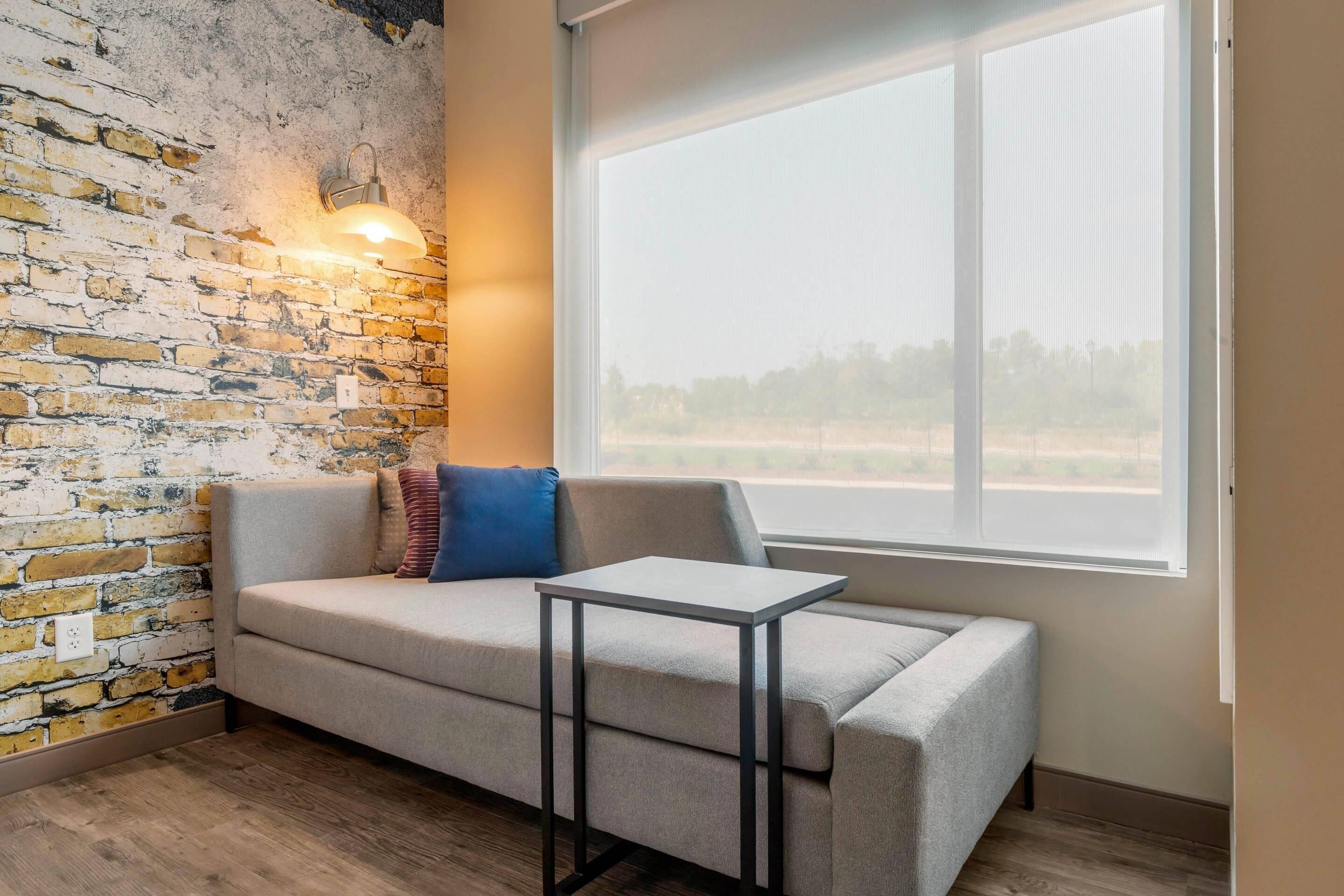 A room with a brick wall, a window, a sofa, and a small table.