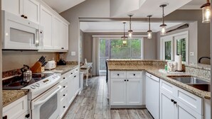 Una cucina moderna con mobili bianchi, piani di lavoro in granito, forno integrato e un'ampia finestra che offre luce naturale.